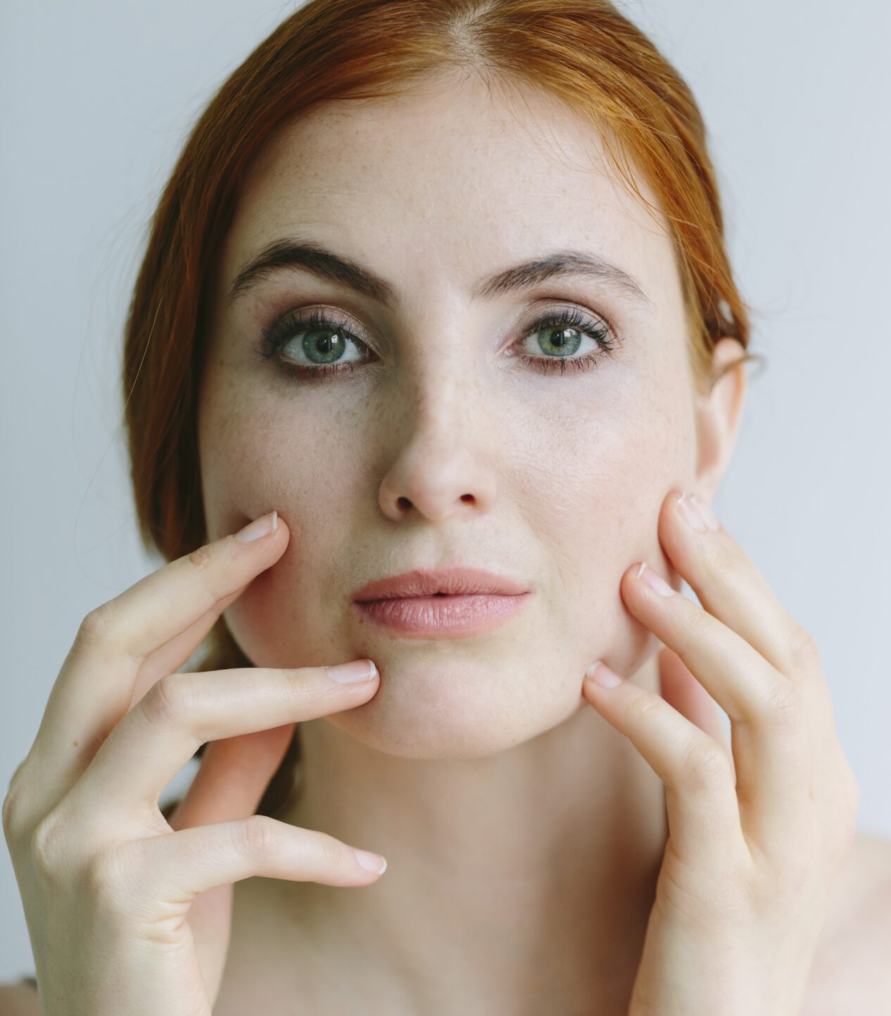 Rothaarige Frau fasst sich fokussiert, prüfend ins Gesicht