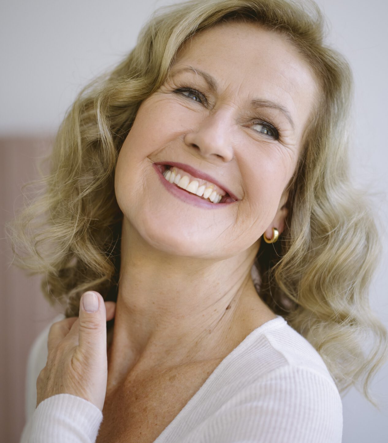 Lächelnde Blonde Frau fasst sich an den Hals